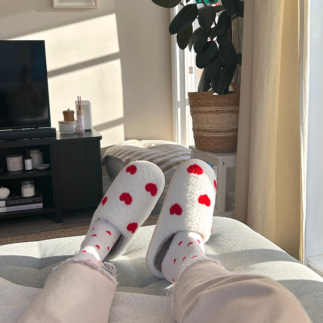 Person wearing fuzzy heart-print slippers relaxing indoors.
