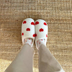 Person wearing heart-patterned slippers and socks on a rug.