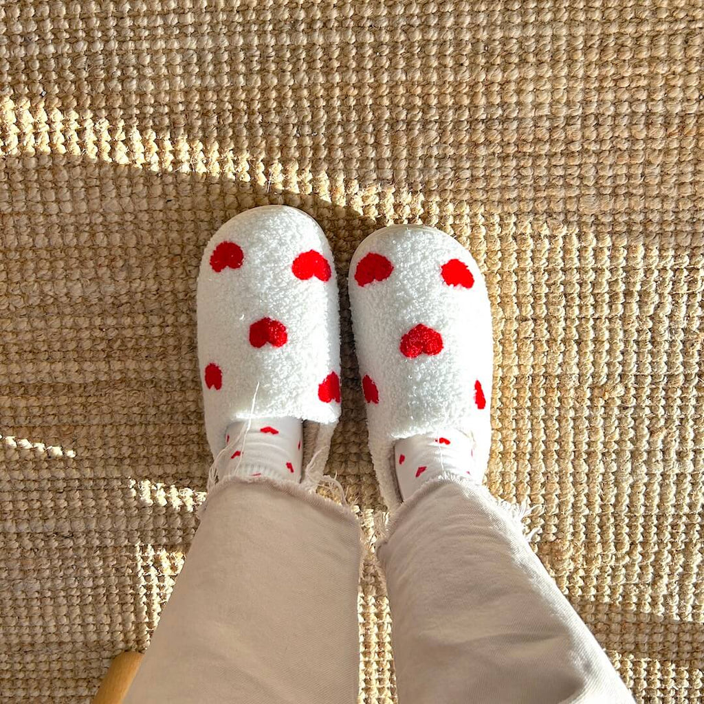Person wearing heart-patterned slippers on a textured rug.