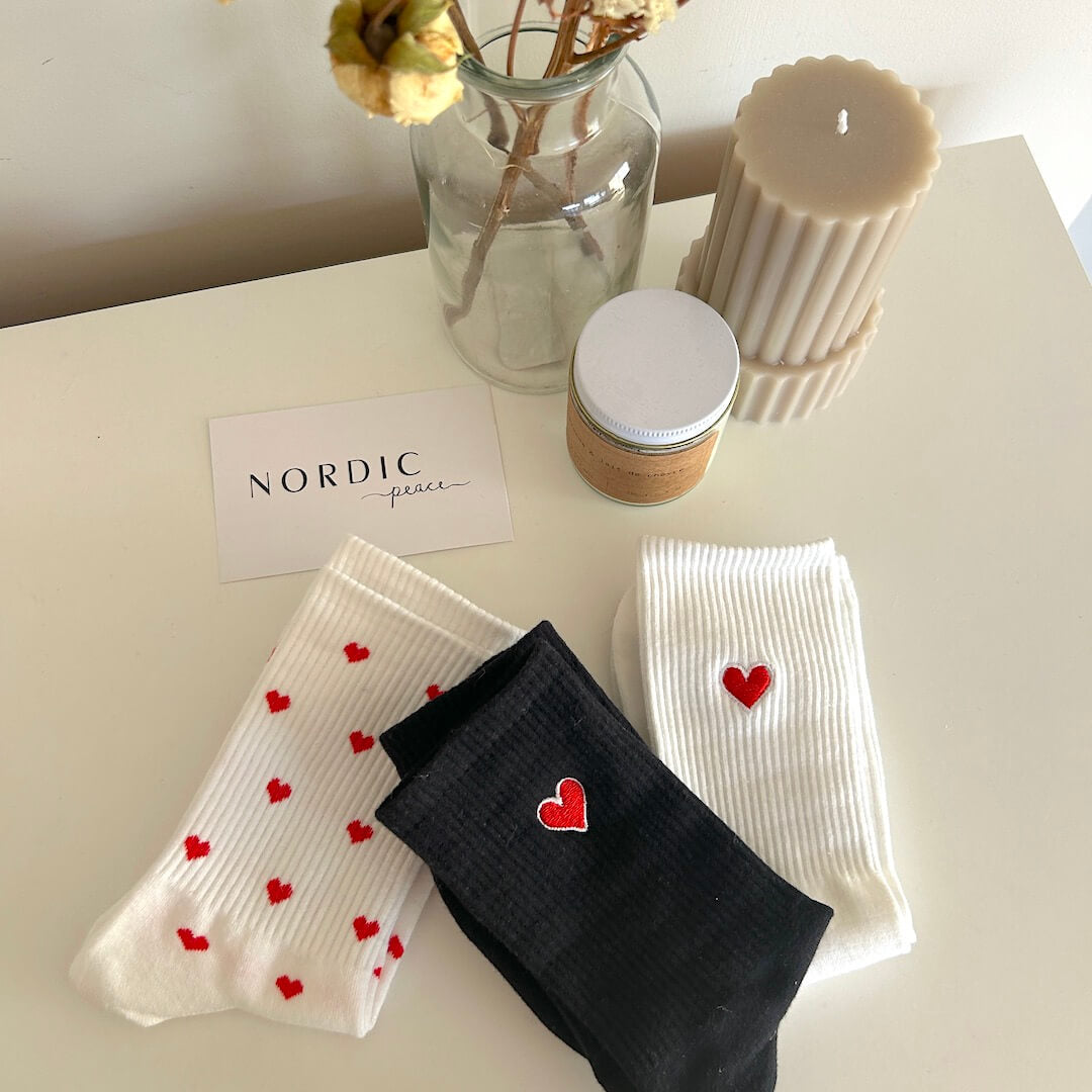 Socks with heart designs, candle, jar, and flowers on a white surface.