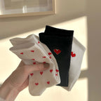 Hand holding three pairs of socks with heart designs.