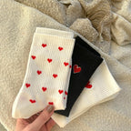 Socks with red hearts on a textured white and black fabric.