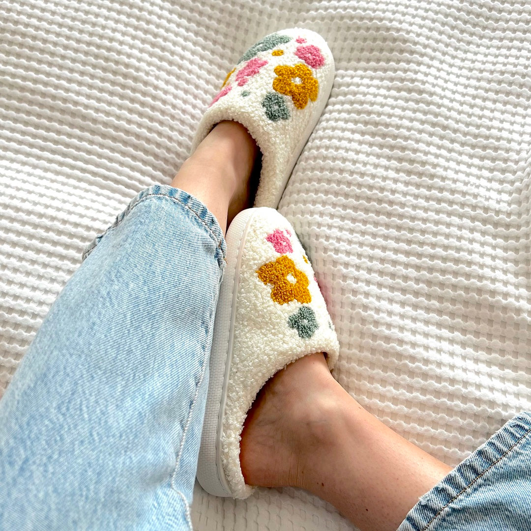 Feet wearing white floral slippers, visible with blue jeans.